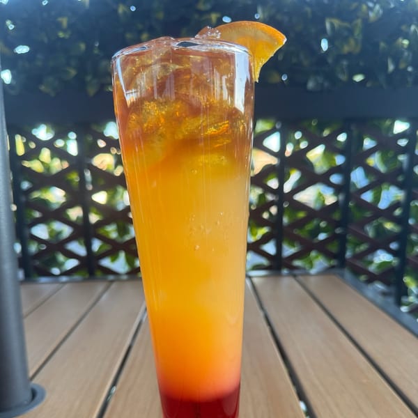 A vibrant Caribbean cocktail with layers of red, orange, and yellow, garnished with an orange slice.