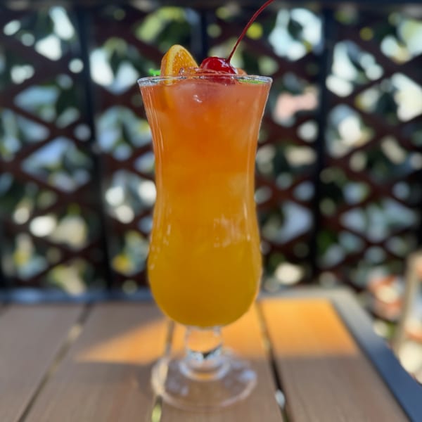 A vibrant Caribbean rum punch cocktail, garnished with an orange slice and cherry, sits on a wooden table.