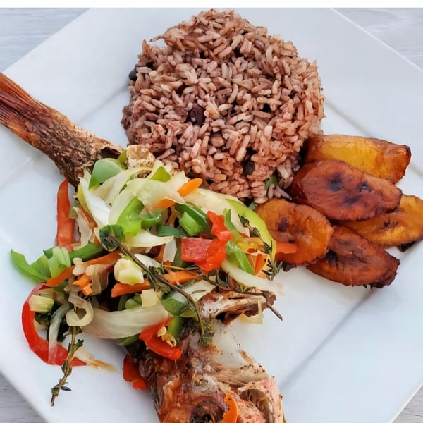 Whole fried fish topped with colorful vegetables, served with rice and fried plantains.