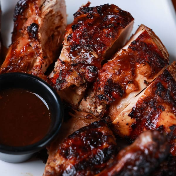 Close-up of Caribbean jerk chicken pieces with glossy sauce and a small bowl of dipping sauce.