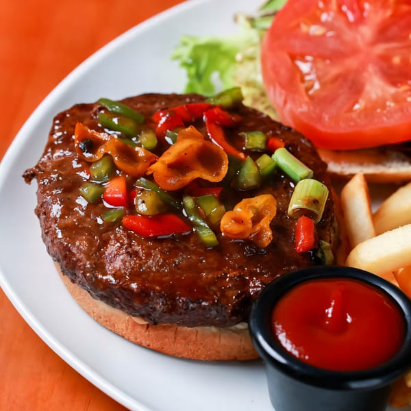 Caribbean burger with colorful peppers, lettuce, tomato, fries, and ketchup on a white plate.
