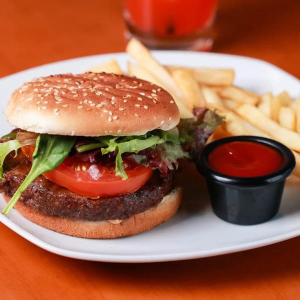 A Caribbean burger with lettuce, tomato, and a side of fries and ketchup on a white plate.