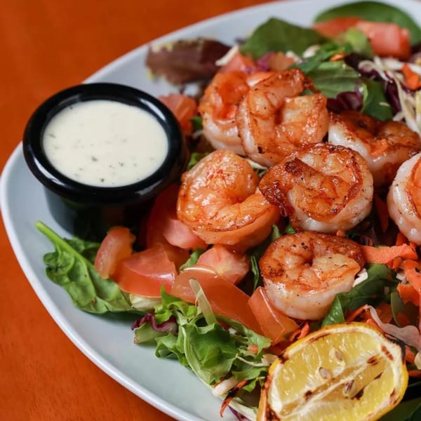 Grilled shrimp salad with mixed greens, tomatoes, and a side of creamy dressing.