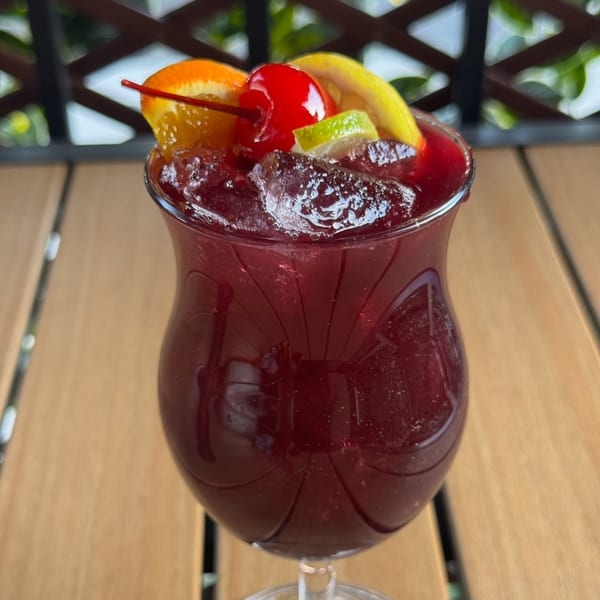 A vibrant red Caribbean cocktail with ice, garnished with orange, lemon, lime, and a cherry.