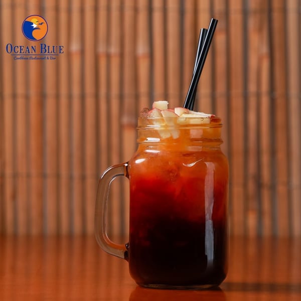 A Caribbean drink in a mason jar with black straws and fruit garnish on a wooden table.