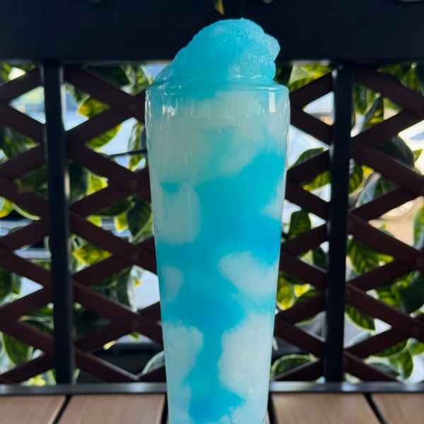 Tall glass of blue and white swirled frozen drink, with a foamy blue top, on a wooden table.