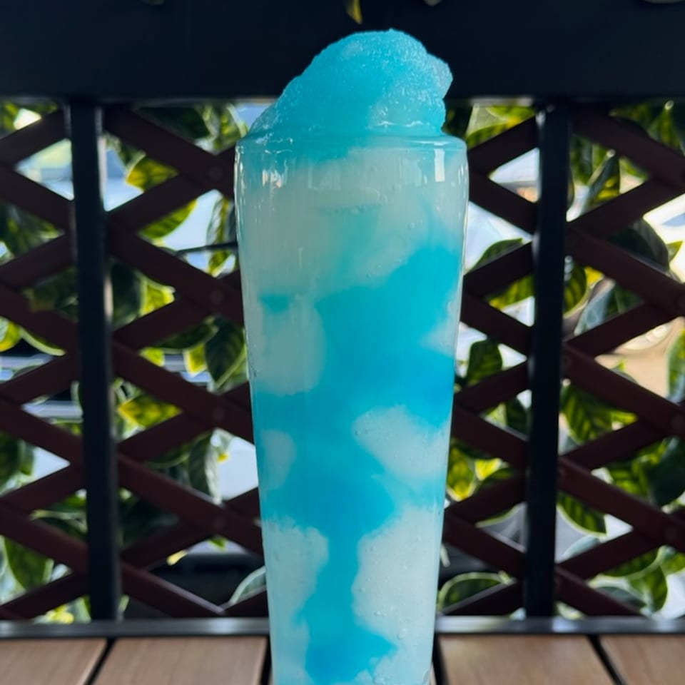 Tall glass of blue and white swirled frozen drink, with a foamy blue top, on a wooden table.