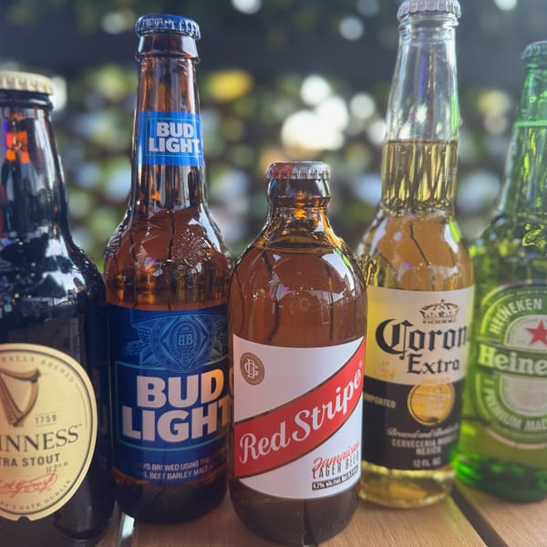 A variety of bottled beers, including Guinness, Bud Light, Red Stripe, Corona, and Heineken, on a wooden surface.