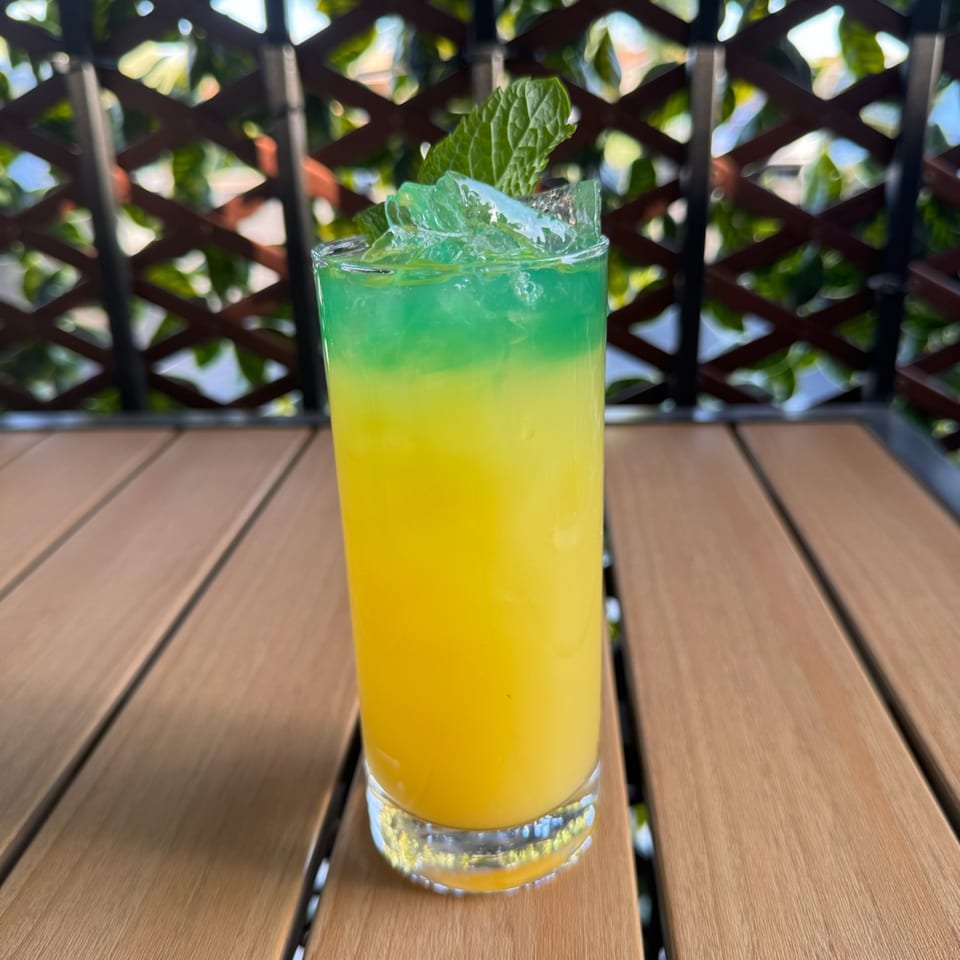 A vibrant yellow and green layered Caribbean cocktail with ice and mint on a wooden table.