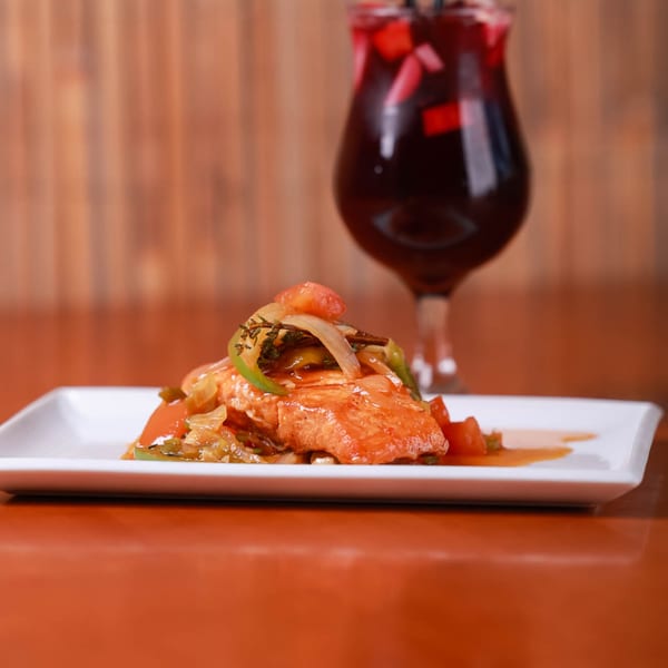 Caribbean chicken or fish entree with peppers, onions, and sauce, served with a red drink.
