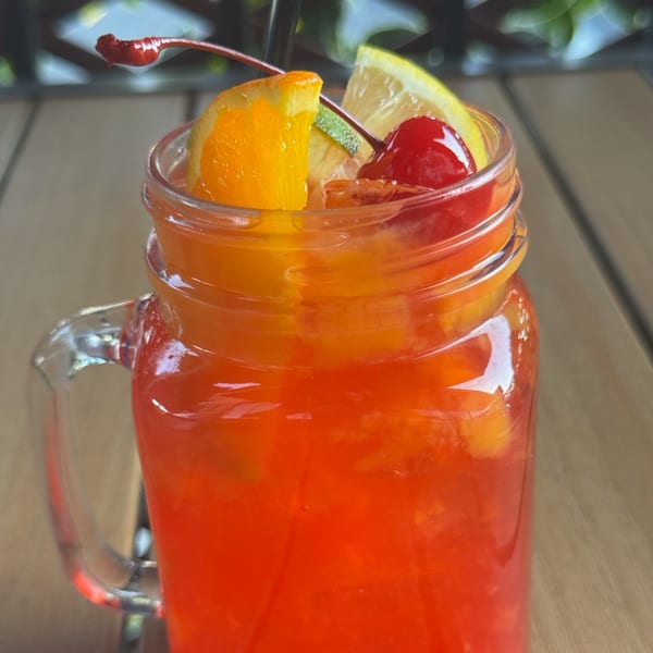 Vibrant red Caribbean cocktail in a mason jar, garnished with orange, lemon, lime, and cherries.