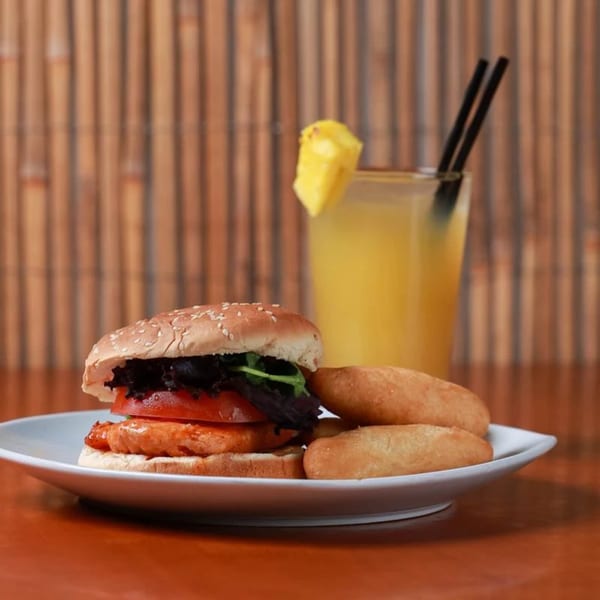 Caribbean jerk chicken sandwich with fried dumplings and a pineapple juice drink.