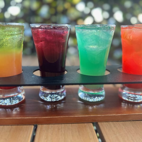 A flight of four colorful Caribbean cocktails, including green, red, teal, and orange drinks.